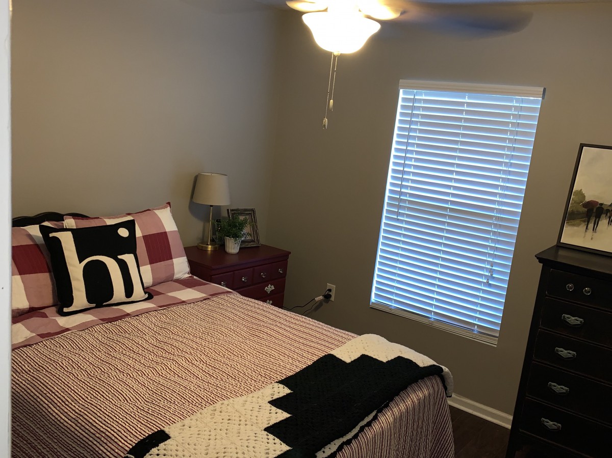 A cozy bedroom with a neatly made bed, a bedside lamp, and a window with blinds.