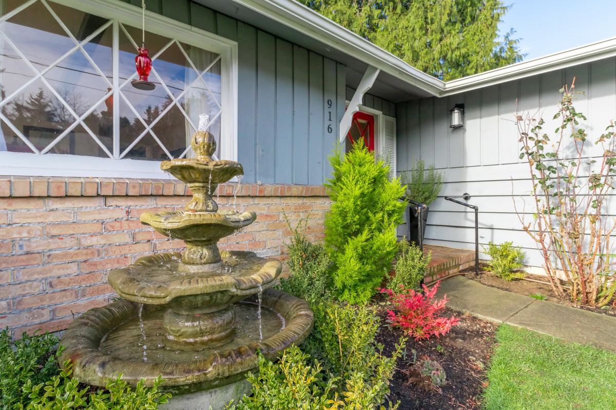 A picturesque front yard featuring a multi-tiered fountain set against a well-manicured garden and house exterior.