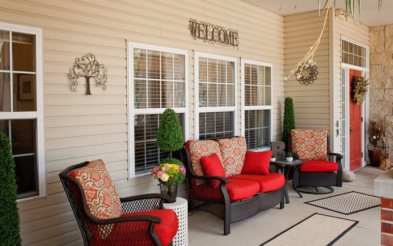A cozy patio setup with wicker furniture and vibrant red cushions, adorned with decorative elements and a welcome sign.
