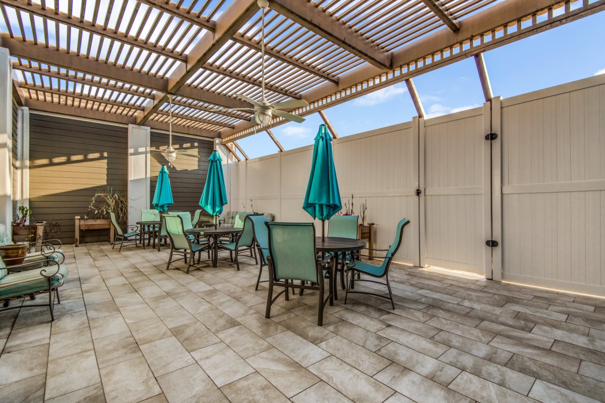 A covered patio area with tables, chairs, and umbrellas under a pergola.