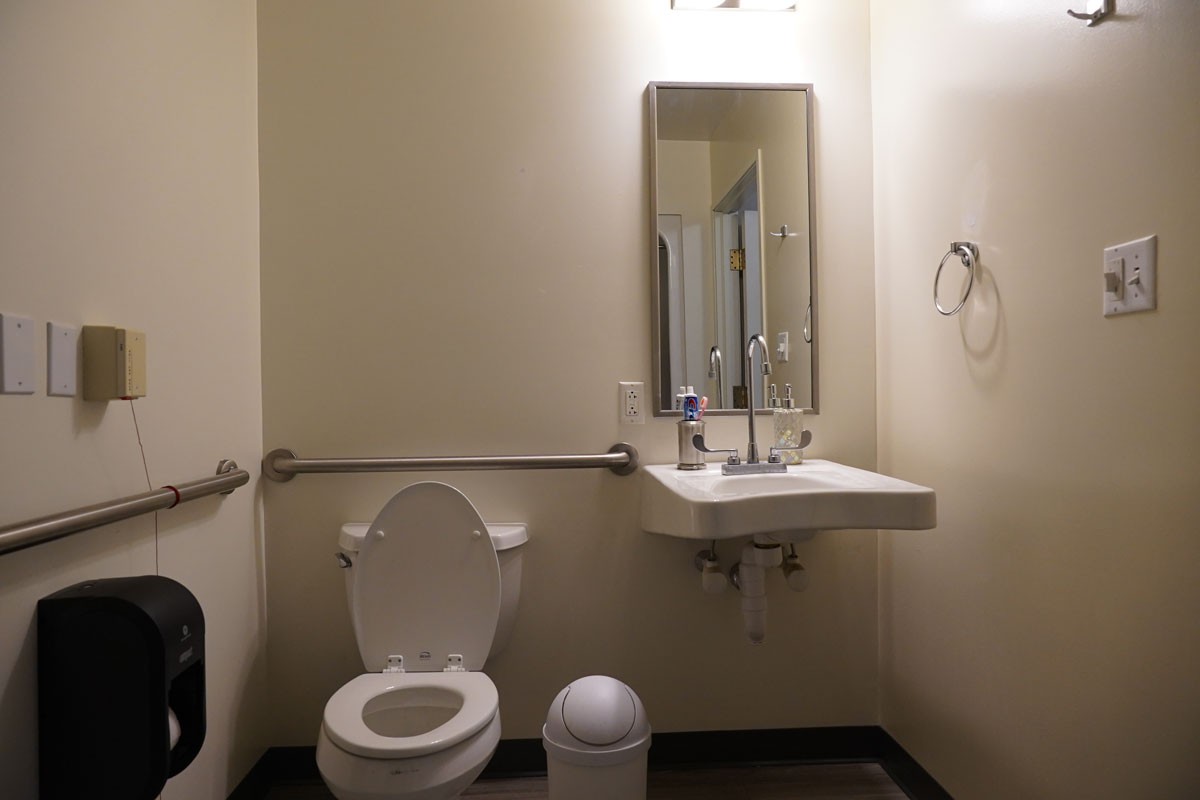 A clean bathroom with a toilet, sink, mirror, and handrail.