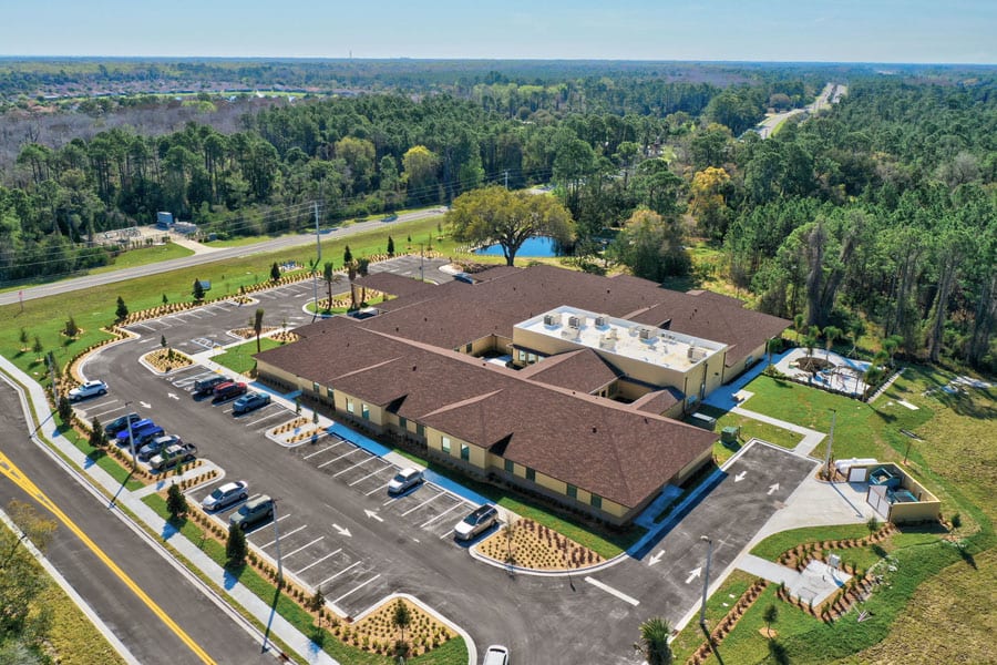 An aerial view of a large building complex surrounded by parking lots and lush greenery.