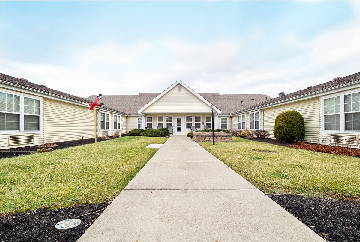 A wide walkway leads to the entrance of a symmetrical residential building, surrounded by well-maintained landscaping.