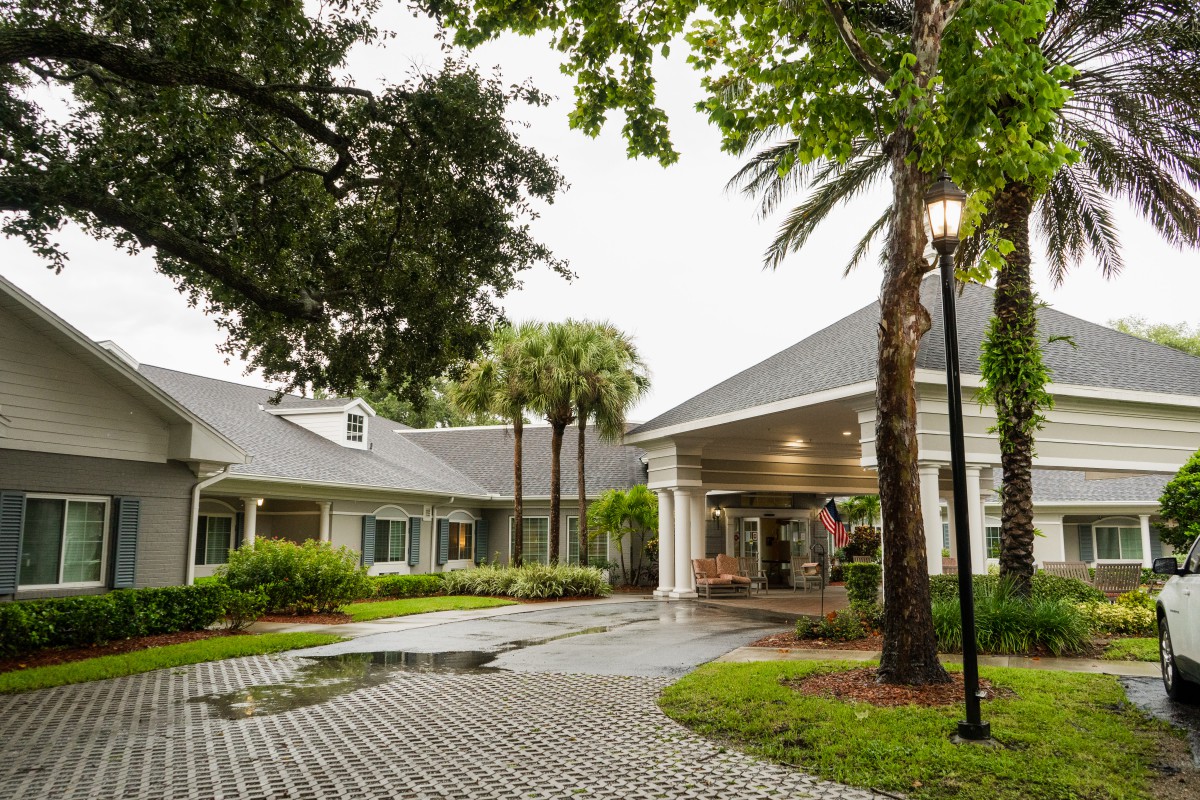 A charming residential building with a welcoming entrance, surrounded by lush greenery and palm trees.