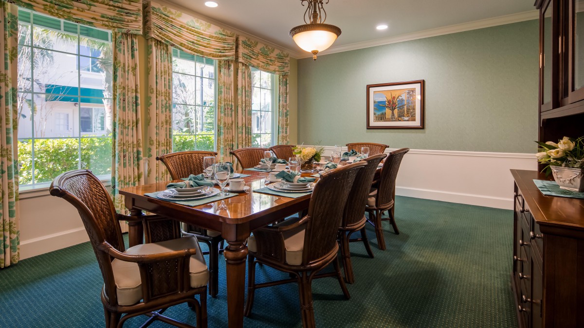 Elegant dining room with a large table set, surrounded by chairs and decorated with curtains and framed artwork.