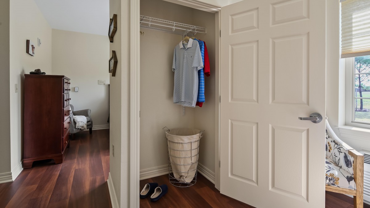 A small closet with clothes hanging, a laundry basket, and shoes on the floor.