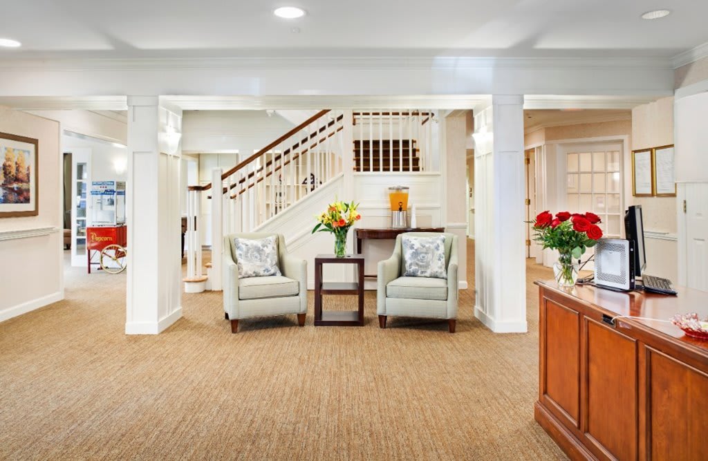 A spacious living room featuring two armchairs, a small table with flowers, and a staircase in the background.