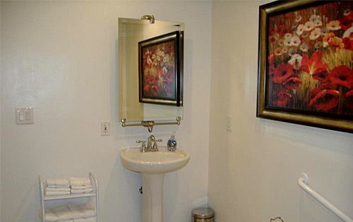 A small bathroom with a pedestal sink, mirror, and framed artwork on the walls.