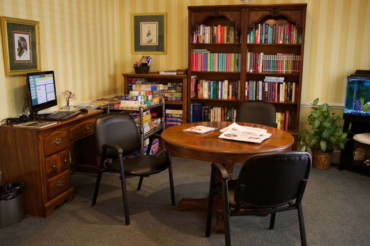 A cozy office setup with a round table, chairs, and bookshelves filled with books.