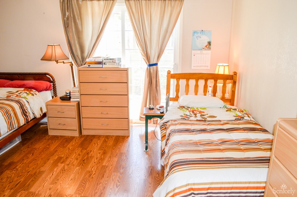 A cozy bedroom with a single bed, wooden floor, and ample natural light.