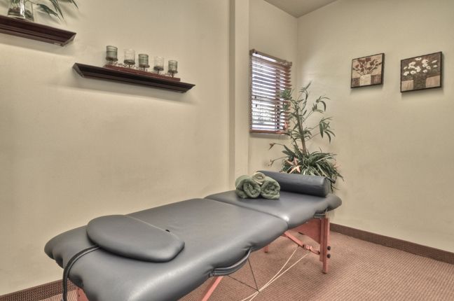 A tranquil spa room featuring a massage table, neatly rolled towels, candles, and a decorative plant.