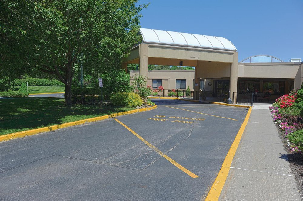A building with a covered entryway and landscaped driveway on a sunny day.