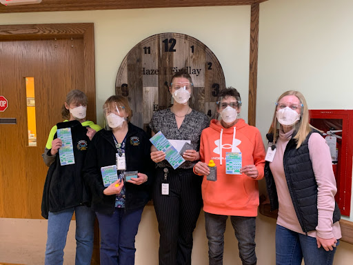 A group of individuals wearing face masks gathers indoors to participate in a community event, proudly displaying items received.