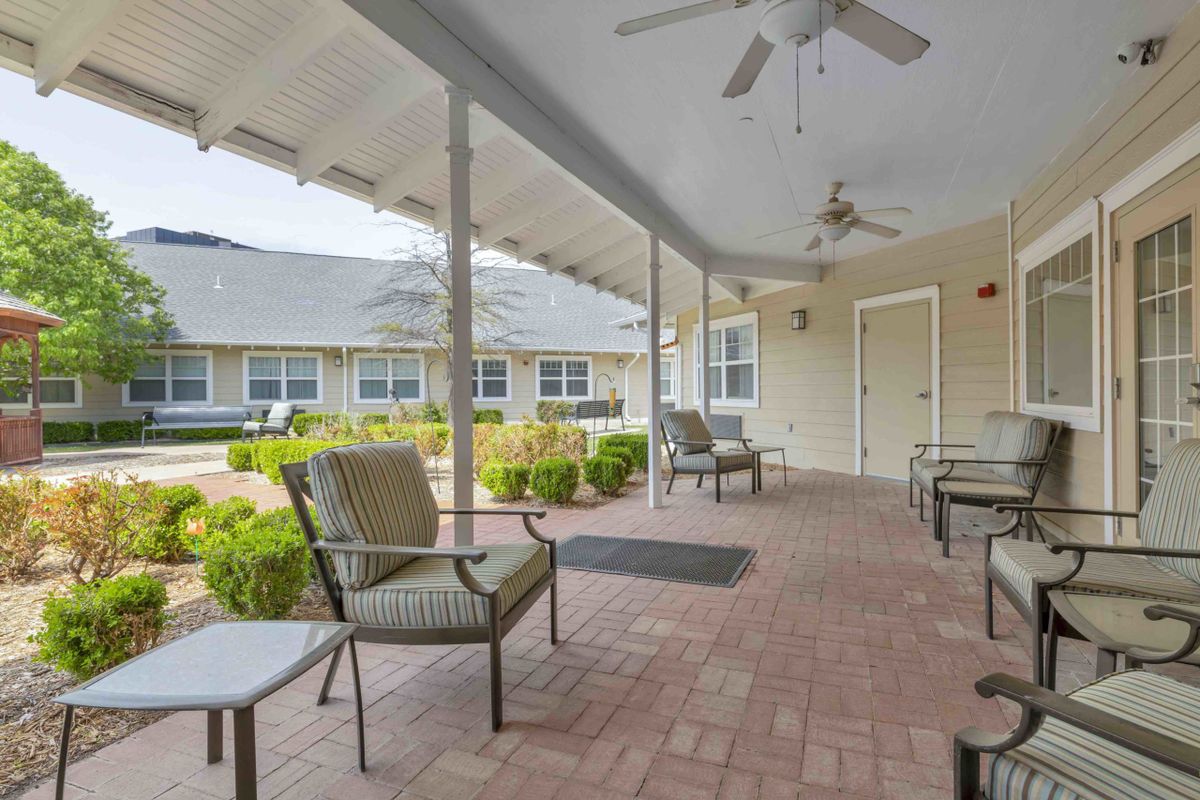 A tranquil patio with comfortable seating and ceiling fans, surrounded by a garden.