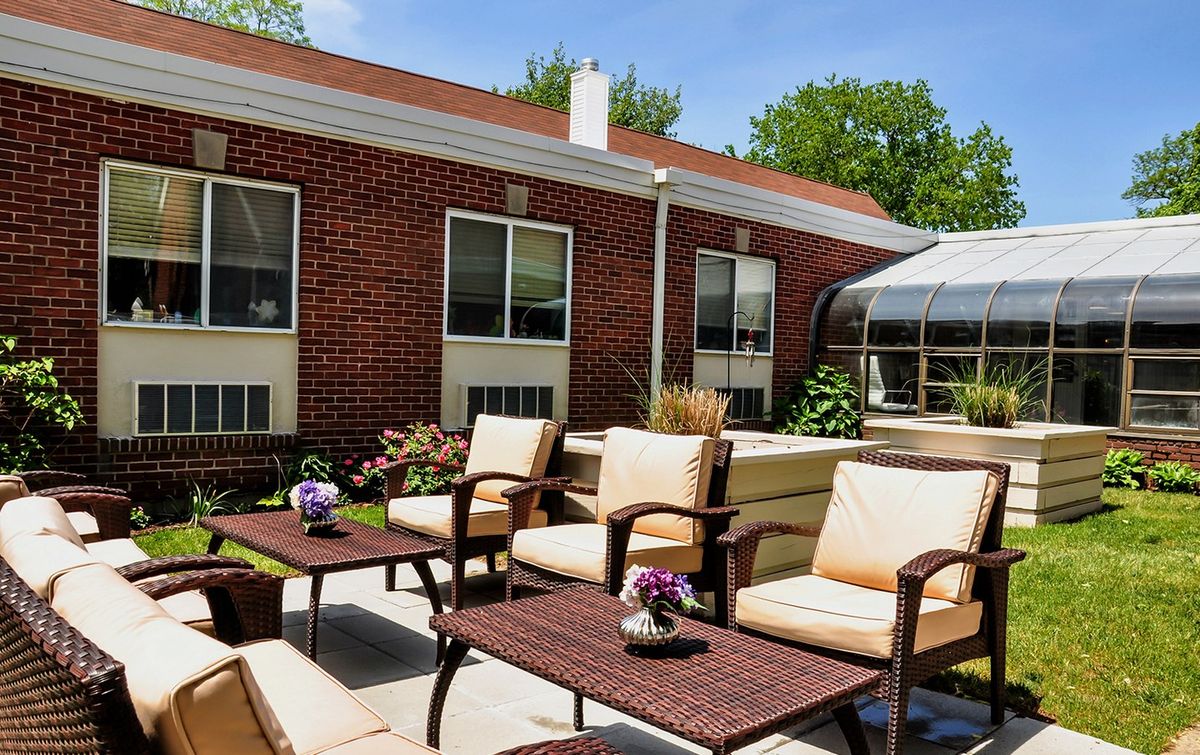 A cozy patio with comfortable seating and tables adorned with flowers, set against a brick building on a sunny day.