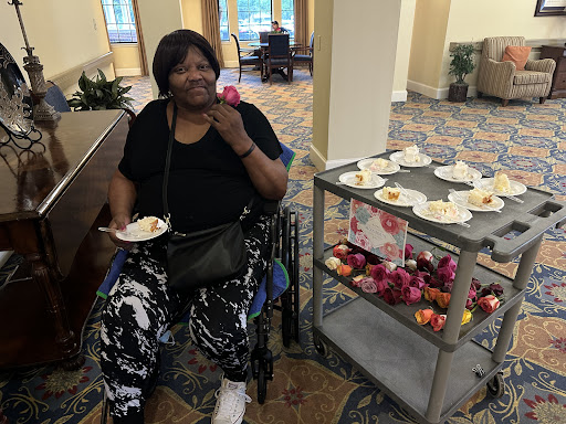 A joyful woman enjoying a treat at a social gathering, seated in her wheelchair beside a food cart filled with snacks.