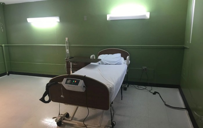 An empty hospital room with a single bed and medical equipment.