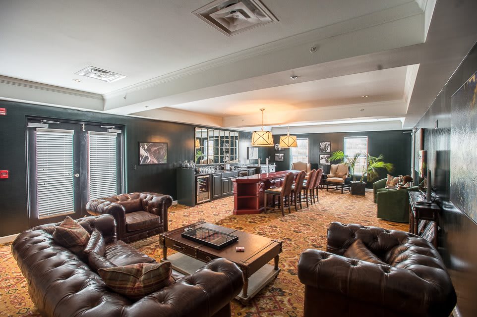 A cozy lounge area with leather sofas, a dining table, and a chandelier, decorated with plants and artwork.