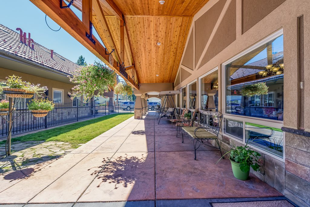 A sunny outdoor walkway with benches and a wooden roof, adjacent to a building.