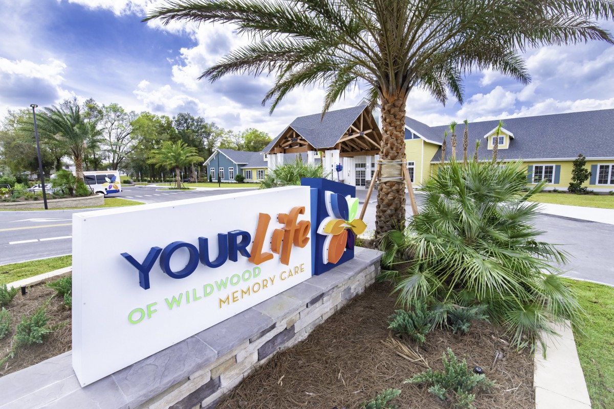 Entrance sign for Your Life facility with palm tree and building in the background.
