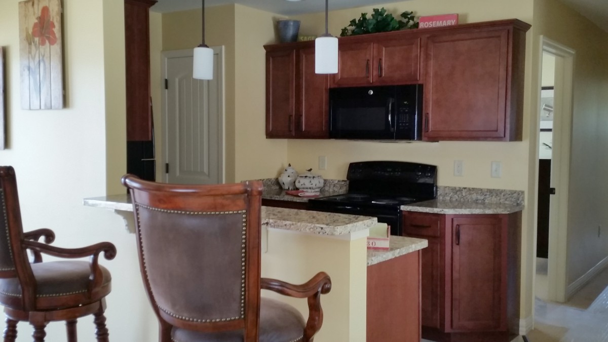 A kitchen interior featuring wooden cabinets, a countertop with bar stools, and modern appliances.