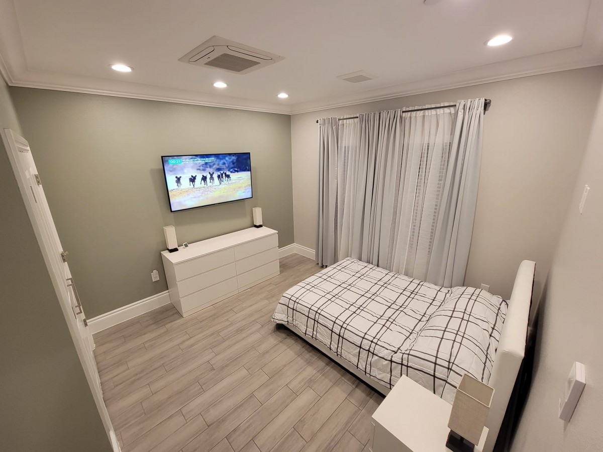 A modern, minimalist bedroom featuring a wall-mounted television and a neatly arranged bed.