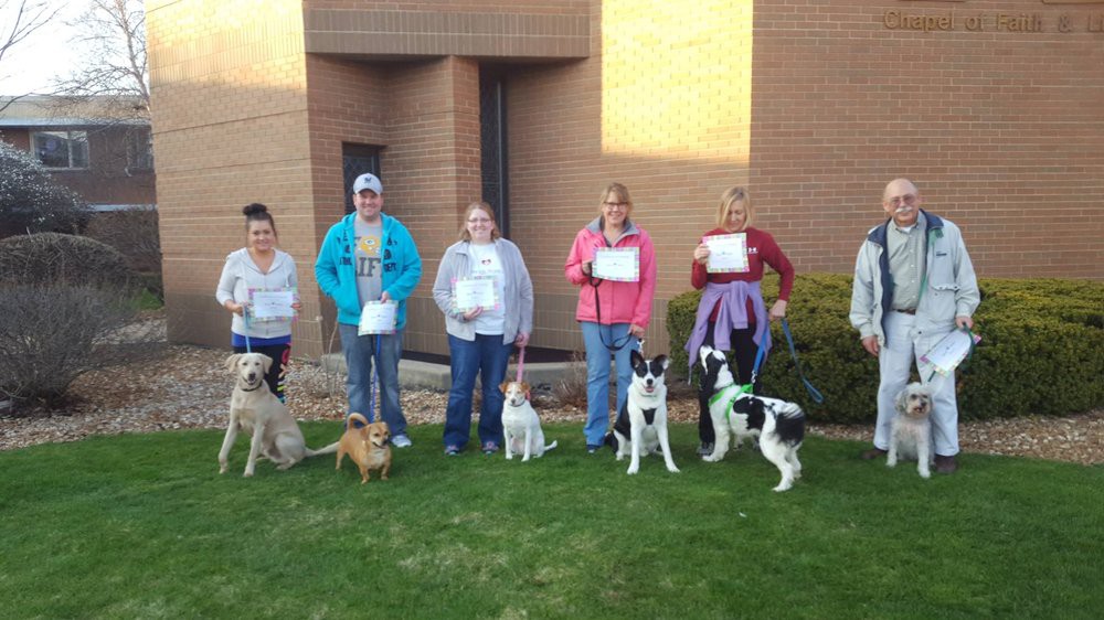A group of people standing outside, each with their dogs and holding certificates.