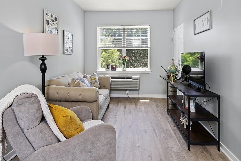 A cozy living room with a sofa, television, and natural light streaming through a window.