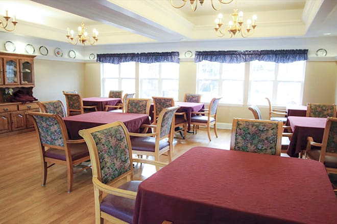 A well-lit dining area with tables and chairs, featuring elegant chandeliers and large windows.