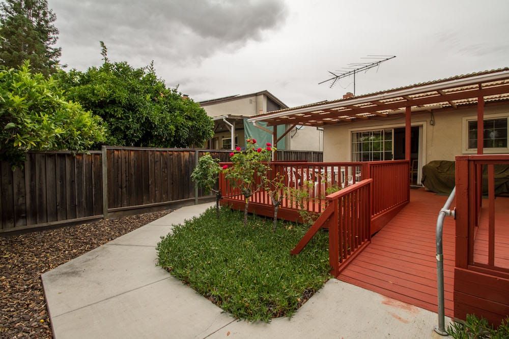 A backyard featuring a wooden deck with an adjacent small lawn and garden, enclosed by a fence.