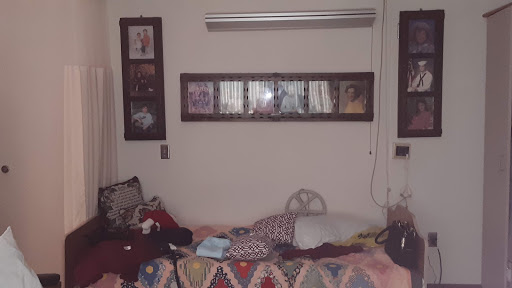 A cozy yet cluttered room featuring a bed, shelves of books or items, and decorative blankets.