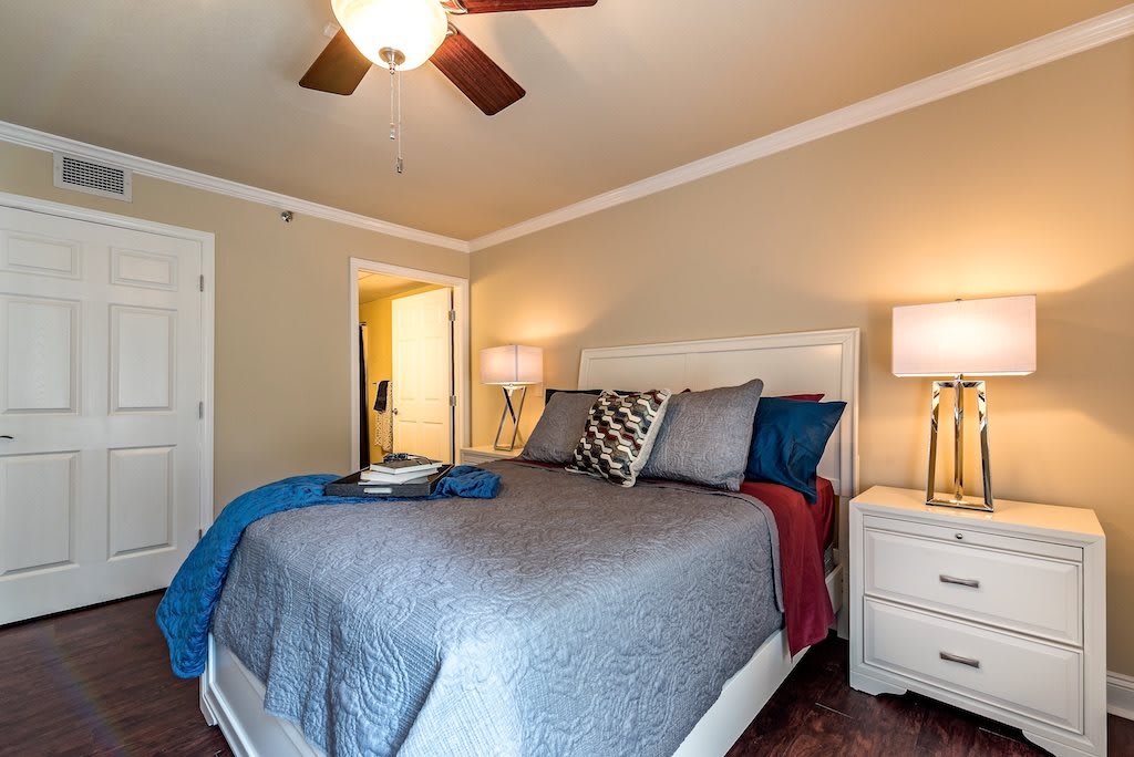 A cozy bedroom with a neatly made bed, ceiling fan, and warm lighting from bedside lamps.