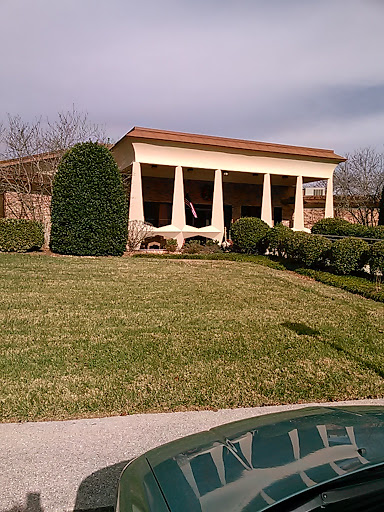 A picturesque building with columns and manicured landscaping, set against a cloudy sky.