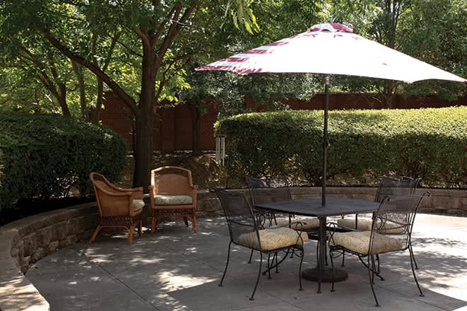 A peaceful patio area with a table and chairs under a large umbrella, surrounded by lush greenery.