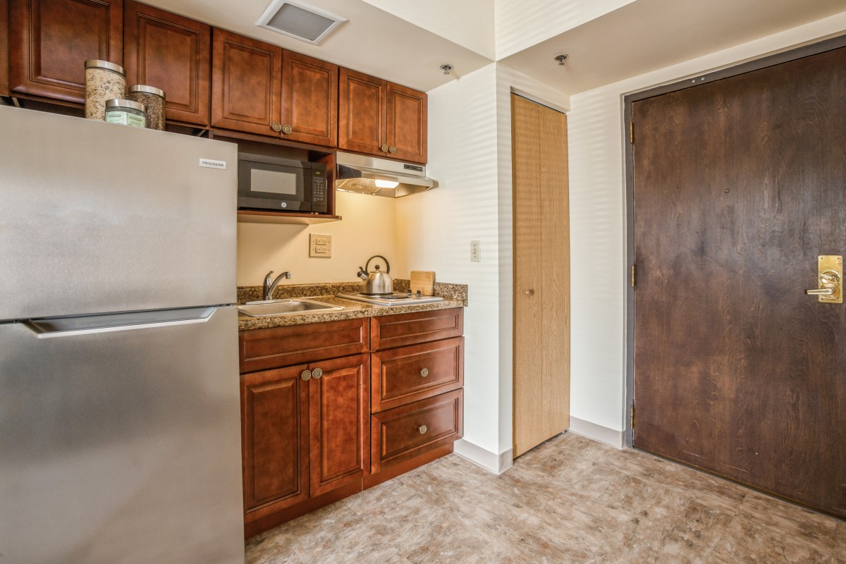 A compact apartment kitchen with wooden cabinets, a refrigerator, and a microwave.