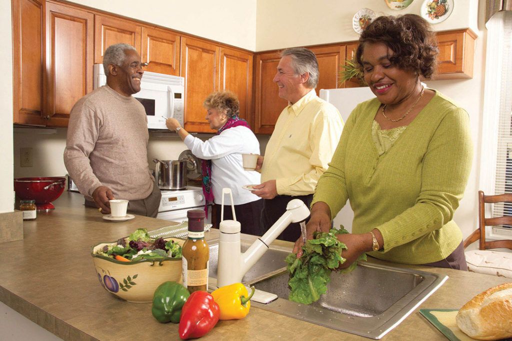 A group of seniors socializing while preparing a meal in the kitchen.