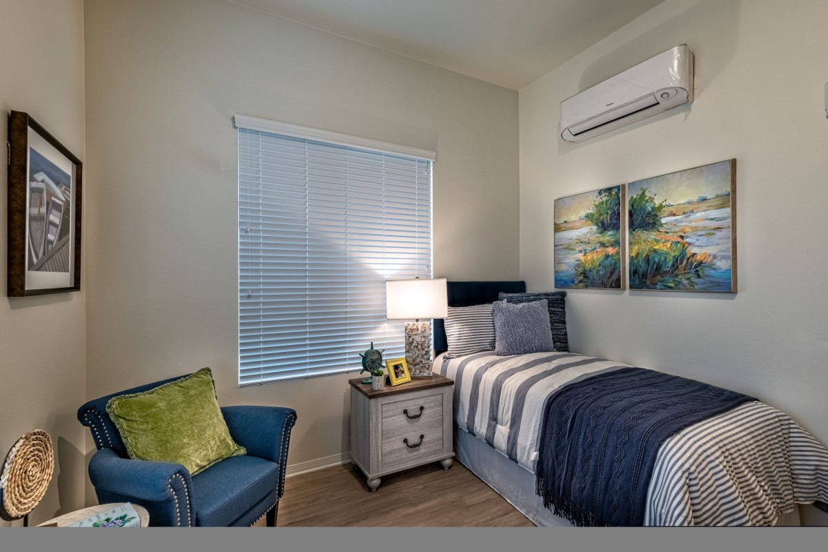 A cozy bedroom featuring a single bed with striped bedding, a nightstand with a lamp, and comfortable seating by the window.