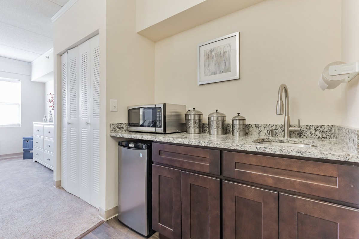 A small kitchenette with a countertop featuring a microwave, mini fridge, sink, and storage cabinets.