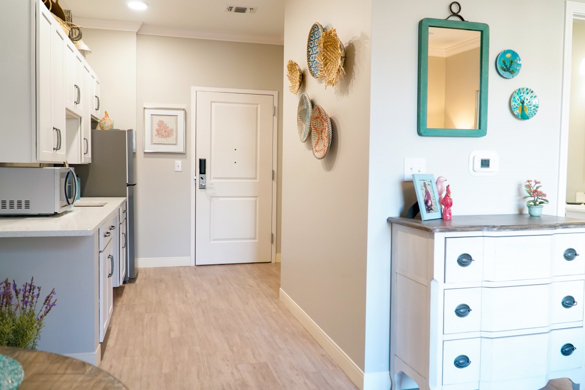 A modern apartment entryway featuring a kitchen with wooden flooring, white cabinetry, and decorative wall art.
