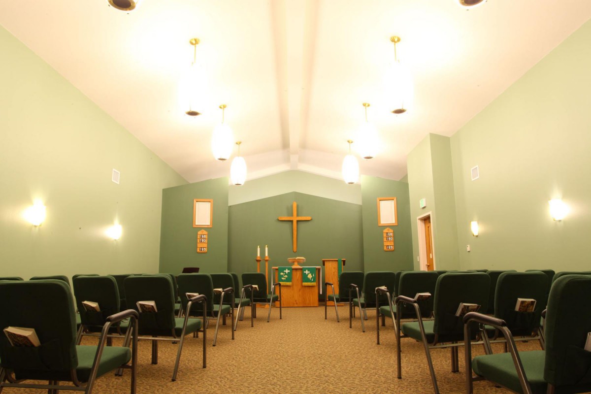An interior view of a chapel with rows of seating and a cross at the front.