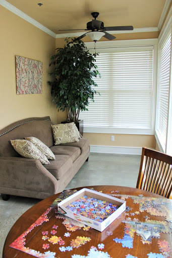A cozy living area featuring a comfortable sofa, a dining table with a puzzle in progress, and natural light streaming through the window.