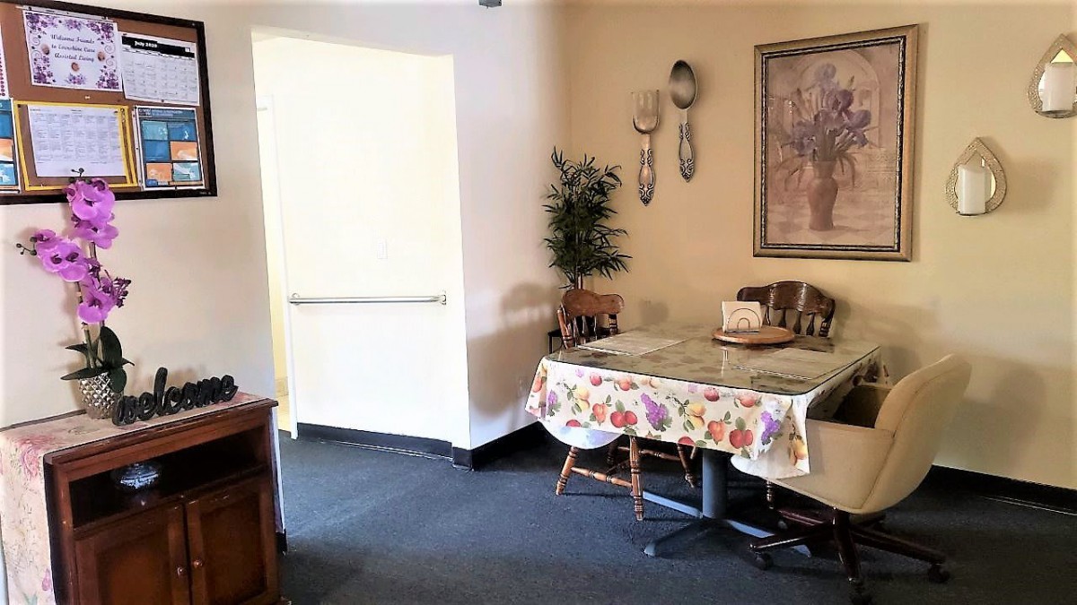 A cozy dining area with a table covered in a floral tablecloth, surrounded by chairs and decorated with wall art and a potted plant.
