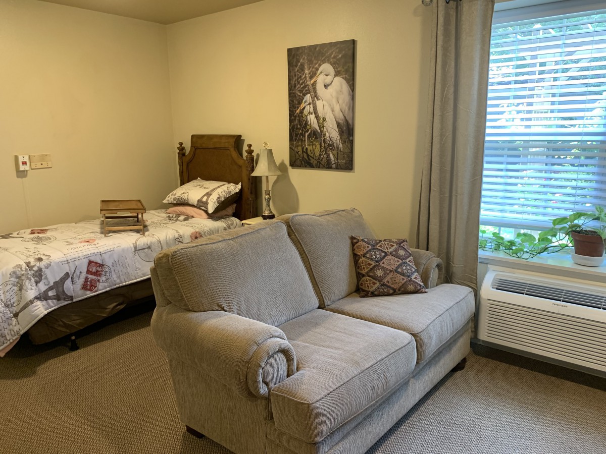 A cozy bedroom features a bed, a couch, and a window with curtains.