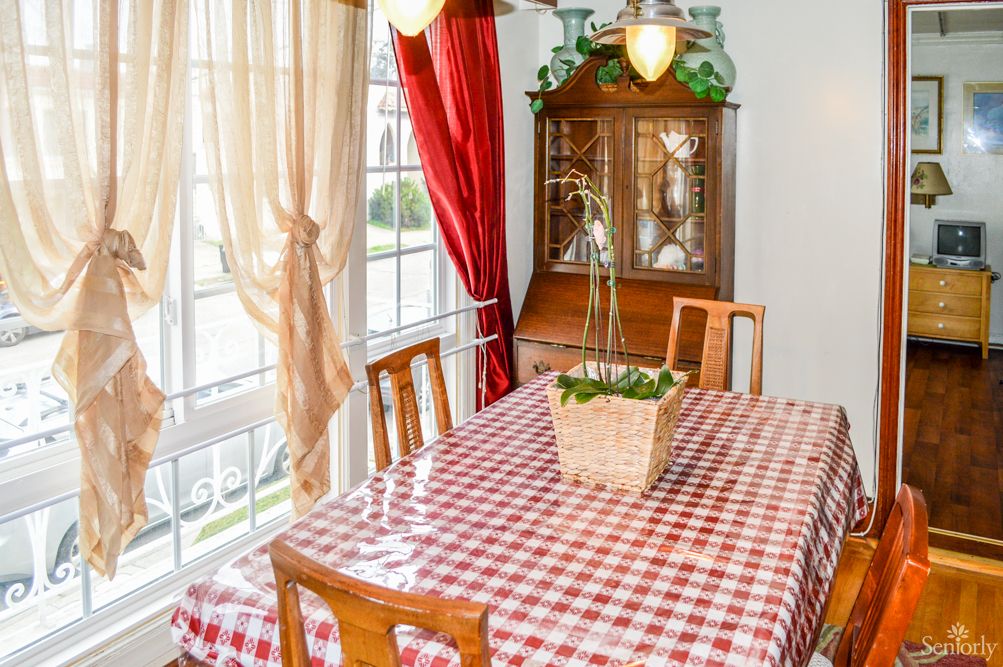 A cozy dining room with a checkered tablecloth, wooden chairs, and a cabinet near the window.