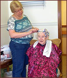 A hairdresser styles the hair of an elderly woman in a salon setting.