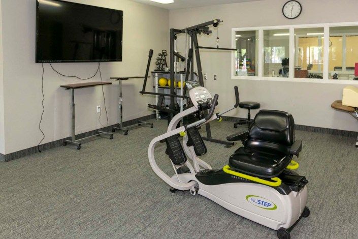 A small gym with various exercise equipment, including a recumbent bike and weight machines.
