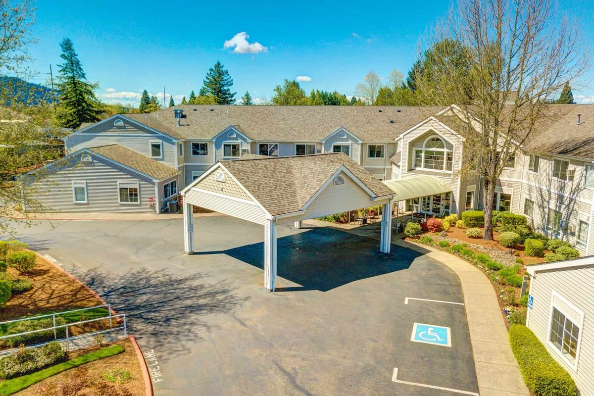 A sunny day view of a residential building with a driveway and parking area.