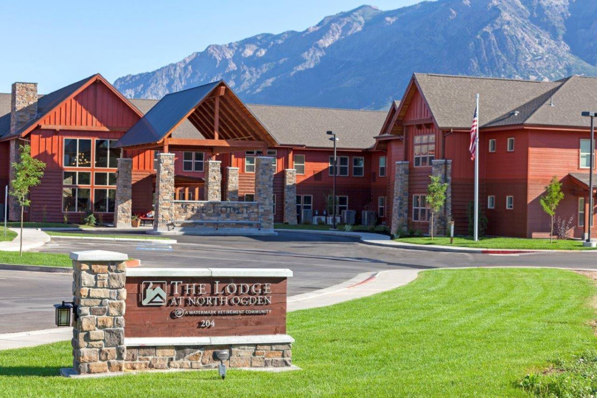 A scenic view of a modern building complex set against a backdrop of mountains, with a sign in the foreground.