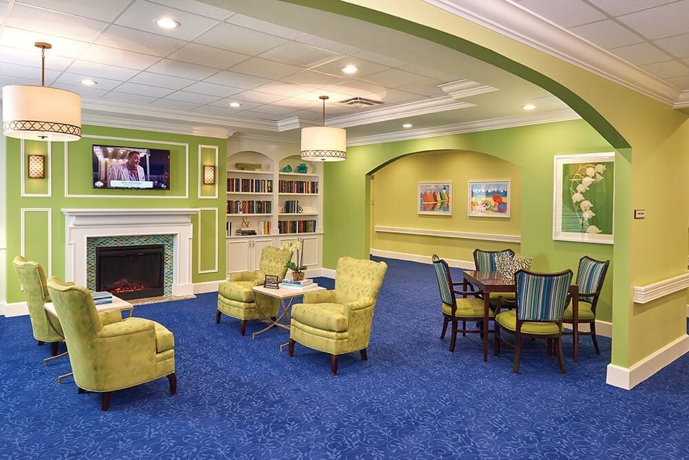 A cozy living room with green walls, blue carpet, and a comfortable seating area around a fireplace.