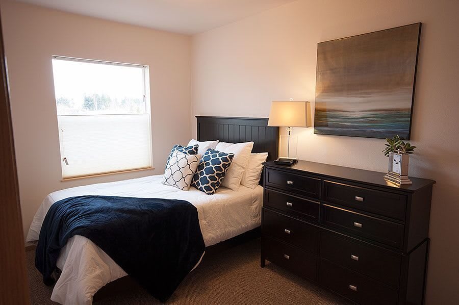 A cozy and well-decorated bedroom featuring a bed with pillows, a lamp on the nightstand, and modern artwork on the wall.